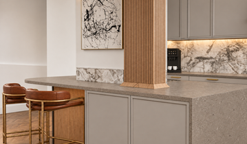 Gramercy Park kitchen island wrapping around a fluted wood column with hidden storage, Silestone Brass Relish countertop, marble accents, and brass-framed stools.