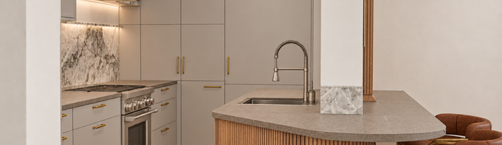 Gramercy Park kitchen with matte European cabinetry, curved fluted wood island, brass hardware, Silestone Brass Relish countertop, integrated sink, and brown leather stools.