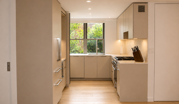 Taupe minimal kitchen with custom millwork cabinetry in Queens, NYC featuring lacquer flat-panel doors, pocket door storage, Thermador appliances, and Dekton countertops. Estimated kitchen investment: $95,000–$110,000.