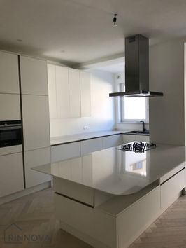 Witte keuken met eiland, moderne apparatuur, en Rinnova in een lichte ruimte.