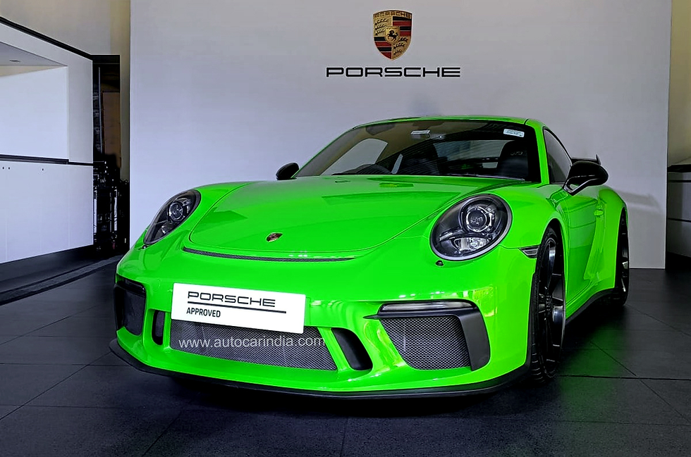 A beautiful green porsche 911 in front of wall with Porsche logo