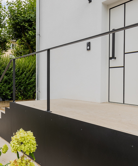 Entrée moderne avec escalier extérieur et rampe noire.