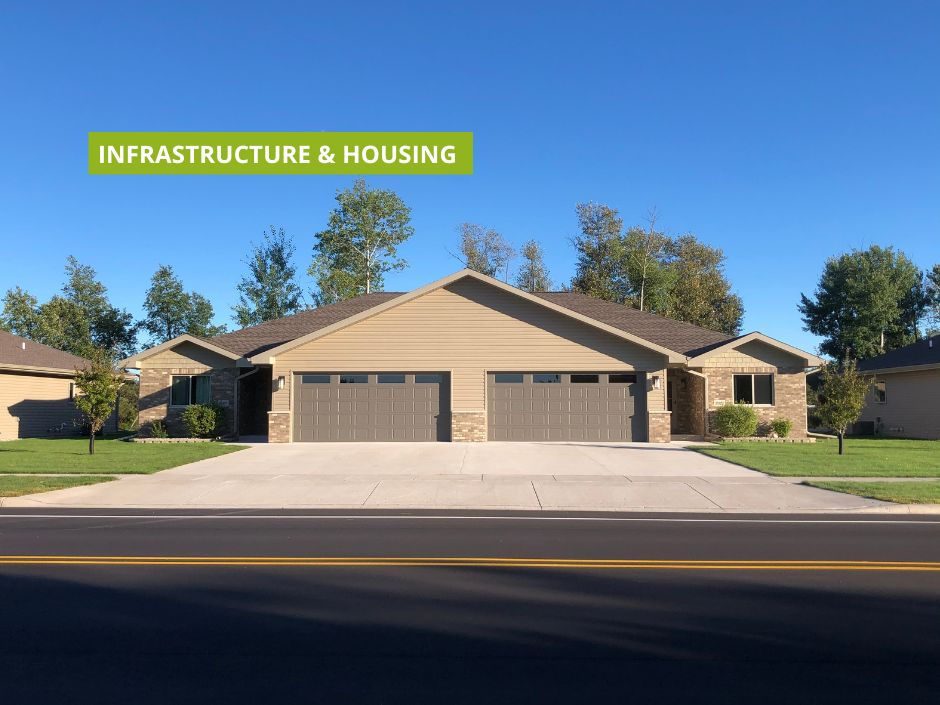Brown duplex house with green lawn and trees against a blue sky. "Infrastructure & Housing" text with a green background.