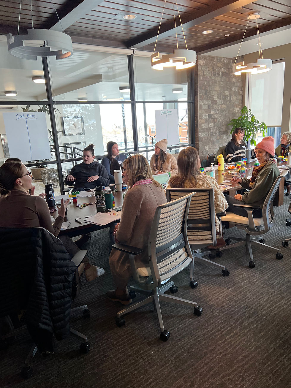 People in a conference room sitting around a table, engaged in discussion. Whiteboards show "Cool Blue" and "Earth Green." Warm lighting.