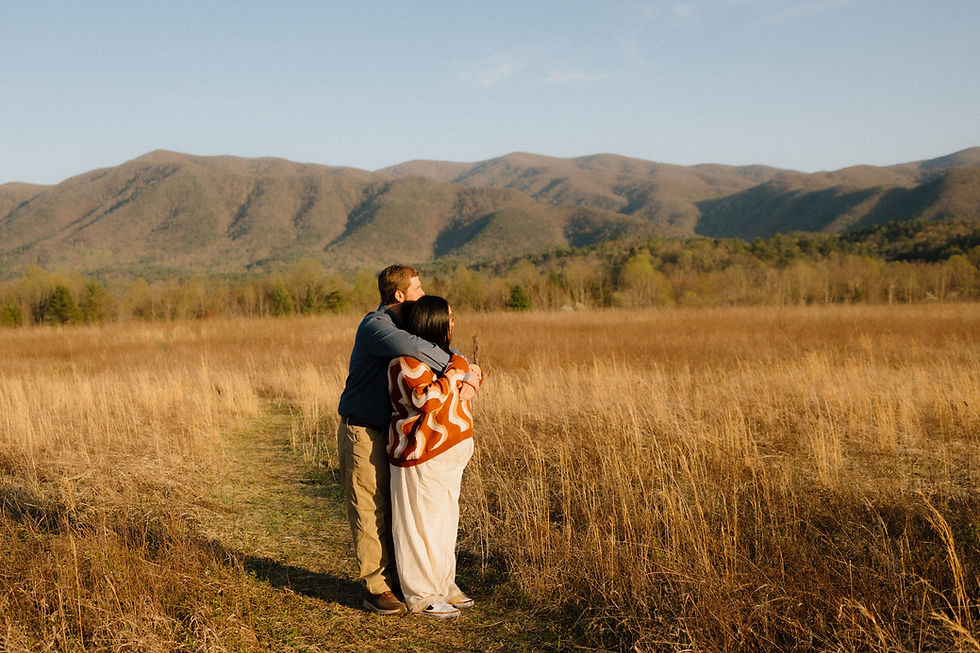 Couple embraces in a golden field with mountains in the background. The sky is clear, and the mood is peaceful and warm.