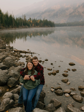 couple smiling in front of alpine lake and autumn trees