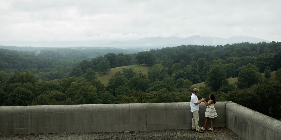 A couple holds hands on a terrace overlooking lush green hills and a cloudy sky, wearing summer outfits. Romantic and serene mood.