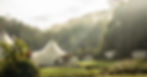 Tents in a misty forested valley, with sunlight filtering through trees. The scene is serene, with green grass and cloudy sky above.