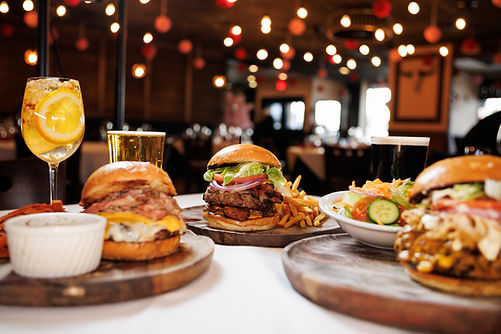 Three burgers, fries, salad, and drinks on a restaurant table
