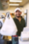 Smiling man holding a white bag, standing behind a counter with a menu.