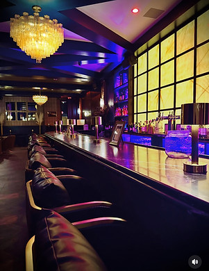 Long bar counter with stools, dim lighting, ornate chandelier, colorful yellow bar.