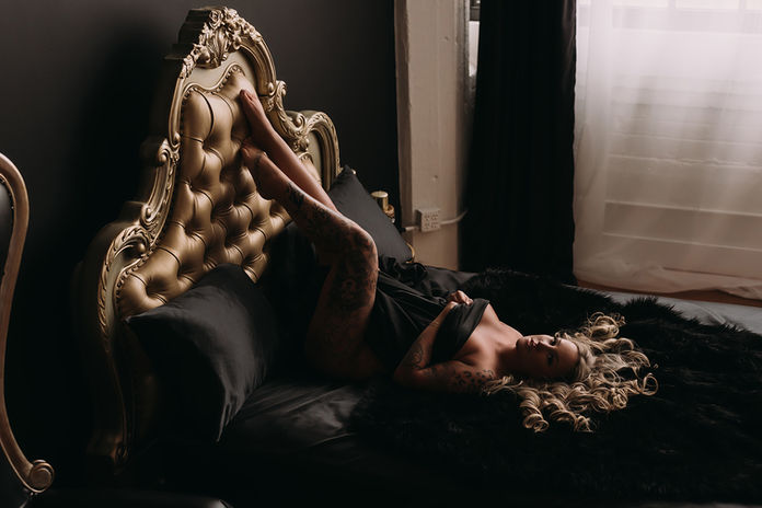 Empowered boudoir client with curly blonde hair and chandelier reflections, posing confidently on gold bed during Cleveland photo session
