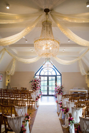 A dramatic broken floral arch in shades of pink and red for a winter wedding ceremony at The Pear Tree at Purton, designed by Wiltshire florist Corky and Prince.