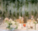 Top table flowers at Kin House with low centrepiece bowl of cream and blush pink roses, bud vases of flowers, white candles and a curtain of flowers and foliage on the back wall