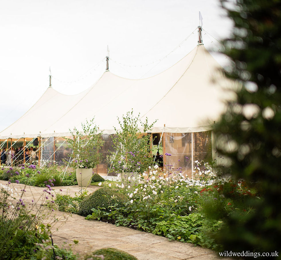 Three pole white marquee in a Cotswold garden with flower borders and trees in pots