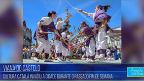 Mulheres com trajes brancos e faixas roxas dançam ao ar livre na Praça da República, em Viana do Castelo, batendo bastões de madeira no ar.