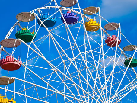 A brightly colored Ferris wheel with red, yellow, green, and blue gondolas set against a clear blue sky, symbolizing the four colour energies of leadership—Fiery Red, Sunshine Yellow, Earth Green, and Cool Blue—from the Insights Discovery model.