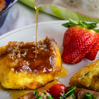 Baked Crème Brulee French Toast and strawberries. Maple syrup is being poured over the French toast 