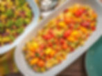 Orzo salad with cherry tomatoes, onions, and herbs on a white platter. Broccoli salad with nuts and cranberries in another dish. Bright setting.