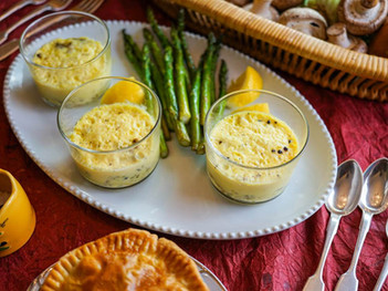 Three glass dishes with soufflé, asparagus, and lemon on a white plate. A basket of mushrooms and pie on red tablecloth. Cozy and inviting.