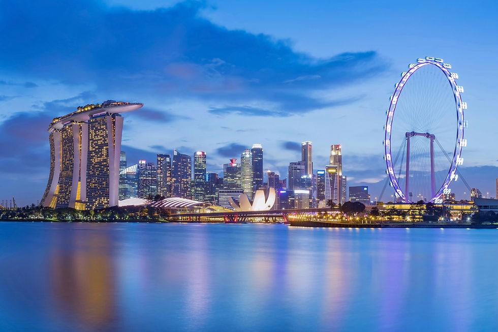 Singapore skyline at dusk with Marina Bay Sands, ArtScience Museum, and illuminated Ferris wheel reflecting on calm water under a blue sky.