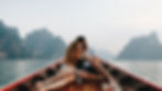 Couple sitting on a wooden boat, holding hands and gazing at serene mountains across a lake. Calm mood with a soft, cloudy sky.