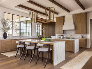 A warm modern kitchen with white oak cabinetry, exposed ceiling beams, and layered natural textures from a custom home designed through close collaboration between architect, builder, and interior designer.