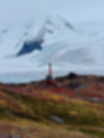 a red helicopter sits on a fall colored mountain in front of a white snowy glacier