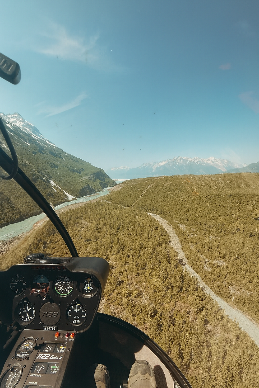 The interior of the cockpit of a Robinson R22 helicopter flying over a river and a lake and some trees in Alaska