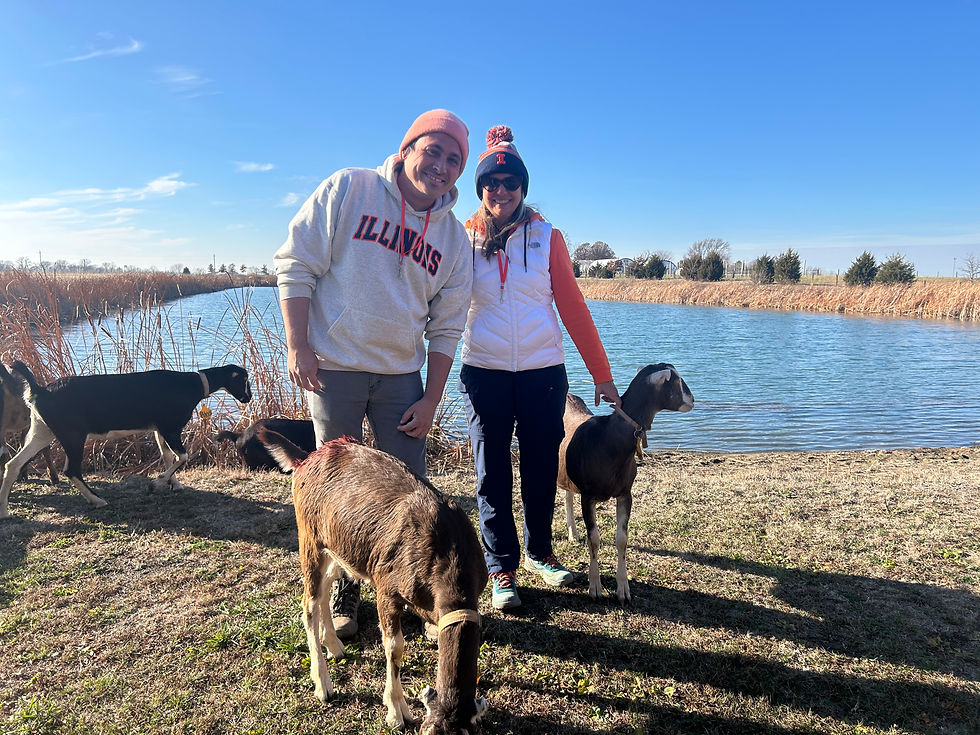 Two people standing in front of a pond with goats