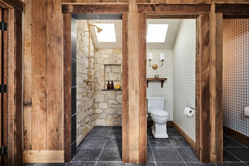 Reclaimed-timber doorways opening to a limestone-lined shower and powder nook over dark slate floors