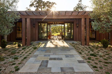 Checkerboard stone paver walkway set in gravel leading to a timber-framed entry pergola