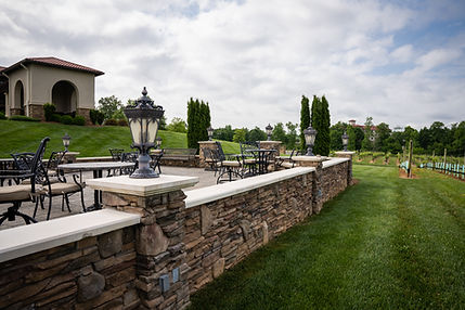 Short intricate stone wall with lamps beside a villa and vineyard. 