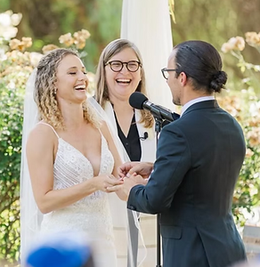 Rabbi Heather Miller officiates a wedding, the couple are smilling and laughing alongside her