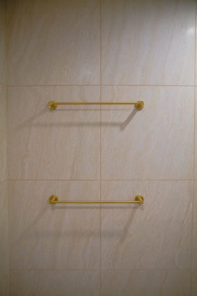 Bathroom renovation Gold Coast featuring brushed brass towel rails installed against warm travertine-look wall tiles