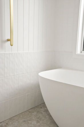 Curved freestanding bath positioned beneath a window in a modern coastal ensuite