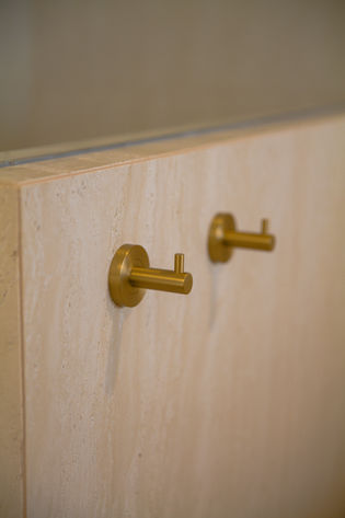Bathroom renovation Gold Coast featuring brushed brass robe hooks installed against warm travertine-look wall tiles