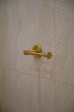 Bathroom renovation Gold Coast featuring brushed brass toilet roll holder detail with warm travertine-look tiled wall finish