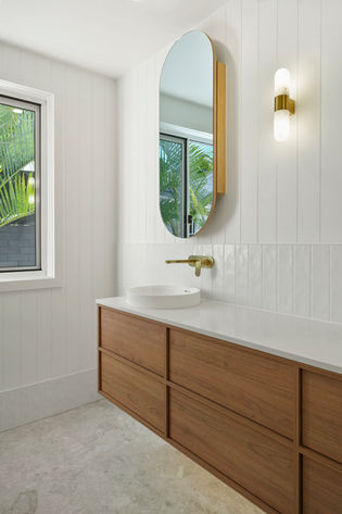 Custom walnut vanity with white benchtop beneath an arched mirror in a modern coastal bathroom