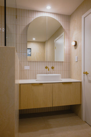 Bathroom renovation Gold Coast showcasing oversized arched LED shaving cabinet with textured feature wall tiles and fluted timber vanity.