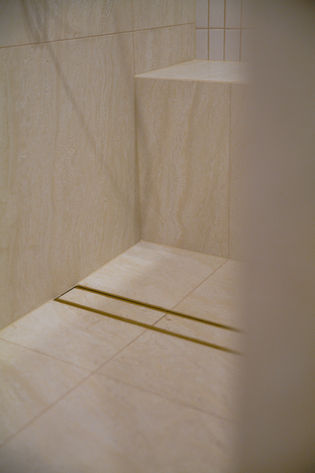 Bathroom renovation Gold Coast featuring custom tiled shower bench and full-height travertine-look wall tiles.