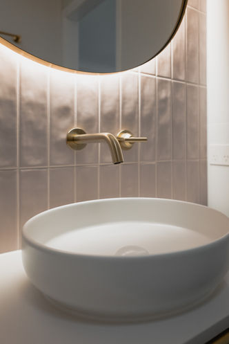 Fluted white vanity set against textured pink wave tile feature wall finished with gold tap ware