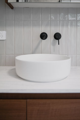 Marble bench top, matte black taps, featuring grey gloss wave feature tile above walnut vanity – Gold Coast renovation.