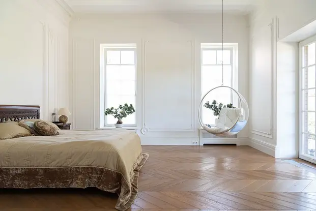 Classic Bedroom with Herringbone Floorboards Dark Wooden Bedhead Frame Beige Quilt Glass Hanging Chair