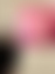 Yi-Chiao Chen in a black coat poses in front of two paintings, one pink and one blue, in a gallery. She smiles, thumb up, against a white wall.