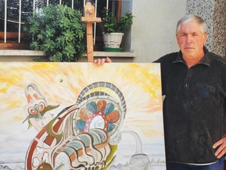 Franco Manià standing beside a colorful abstract painting with sunset colors and intricate designs, outside by a window with plants, looking serious
