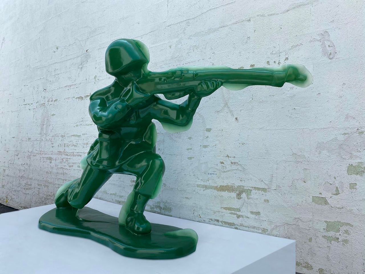 Green fiberglass sculpture of a toy soldier in kneeling position with a rifle, examining themes of militarism and childhood.