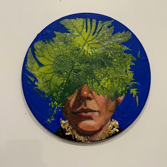 Painted portrait of a face partially covered with green leaves, against a deep blue circular background. Gold accents adorn the neck.