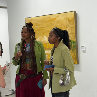 Two guests holding drinks and chatting in front of a large yellow-toned painting