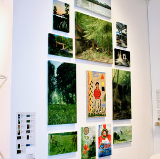 Installation wall featuring green landscape-inspired artworks and smaller orange-toned pieces